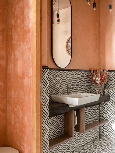 Terracotta plastered powder room with oval mirror, bare bulb pendants, and geometric tiled vanity wall