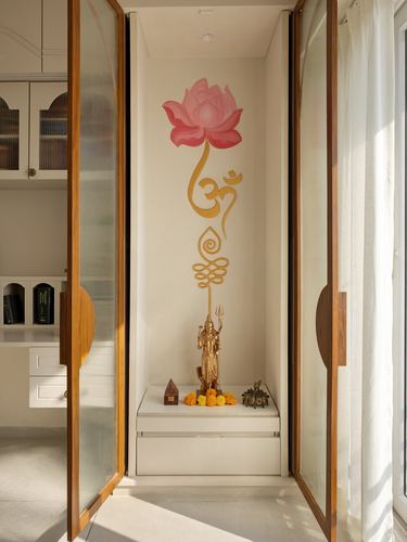 Pooja niche with brass Shiva idol, marigold garland, and hand-painted lotus mural, framed by fluted glass doors