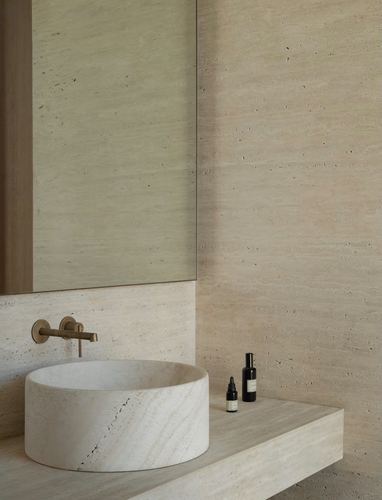 Travertine bathroom with round stone basin, brass wall-mounted faucet, and mirror