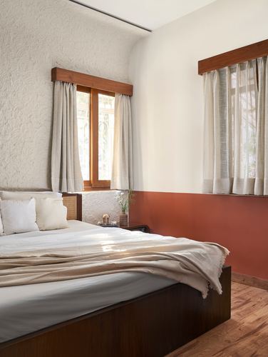 Bedroom corner with terracotta-and-cream wall, cane headboard bed, two curtained windows