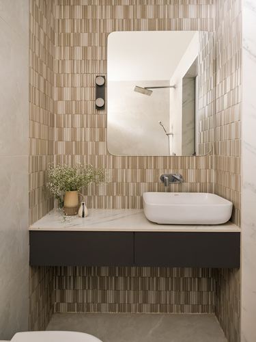 Bathroom vanity with vessel sink, mirror reflecting shower, and fluted tile wall in warm tones