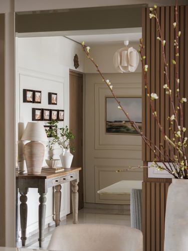 Foyer view through wood slat partition into a paneled hallway with console table, lamp, and gallery frames