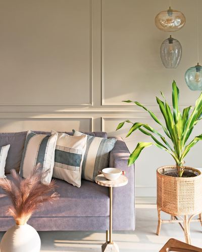 Lavender sofa with striped cushions beside rattan planter and hanging glass pendant lights against panel-moulded wall