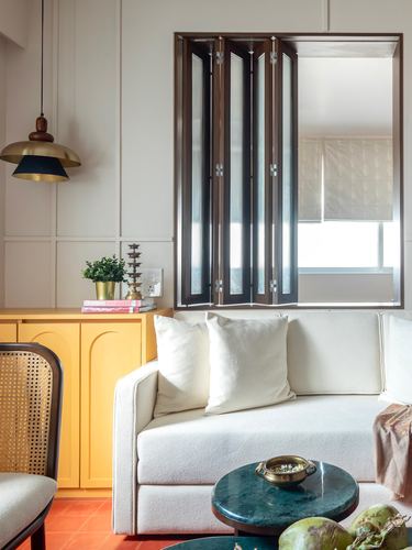 Living room corner with cream sofa, folding wooden shutters, mustard cabinet, and green marble table
