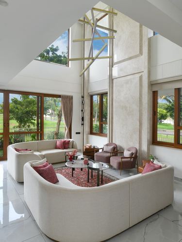 Double-height living room with curved cream sofas, pink armchairs, and a sculptural hanging light under a sloped ceiling.