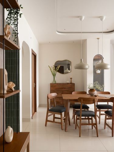 Wood dining table with cane-backed chairs under mismatched pendant lights beside a wooden sideboard and mirror