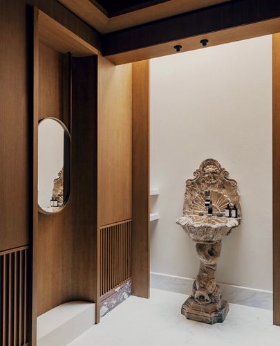 Ornate antique carved stone basin sculpture set against plain wall, framed by wood-paneled corridor