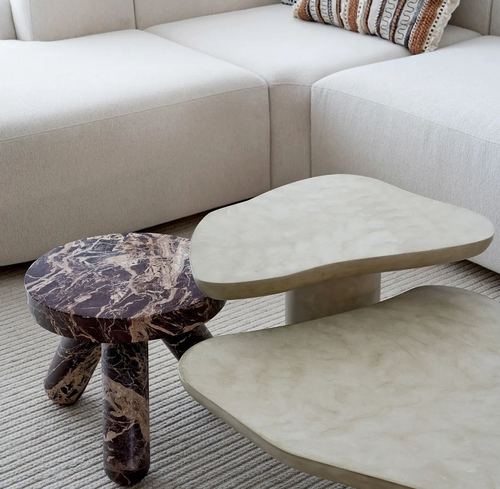 Dark marble tripod side table beside two freeform cream tables in front of a beige boucle sofa