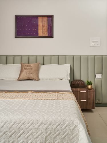 Bedroom corner with sage tufted headboard, walnut nightstand, and framed purple textile above bed
