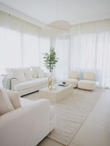 All-white living room with sheer curtains, two sofas, barrel chairs and a sculptural pendant light
