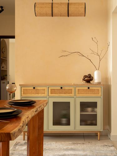 Sage-green cane and wood sideboard against warm plaster wall with cane pendant light and dining table