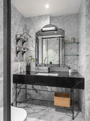 Marble bathroom with black stone vanity, arched mirror, and wicker basket below