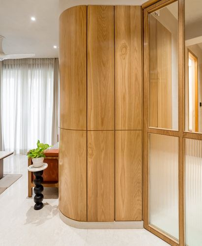 Curved wooden cabinet beside a reeded glass door in a marble-floored foyer