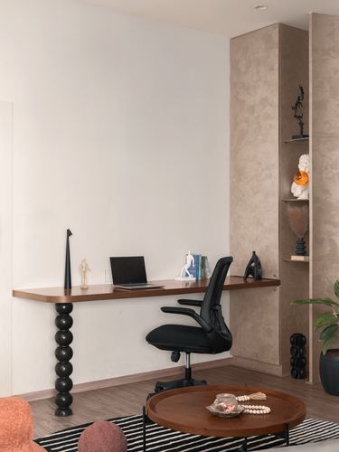Wall-mounted wooden desk with black ergonomic chair beside a textured stone display niche