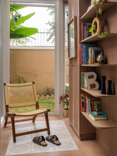 Cane chair on patterned tile by glass door, wooden shelving with books beside it