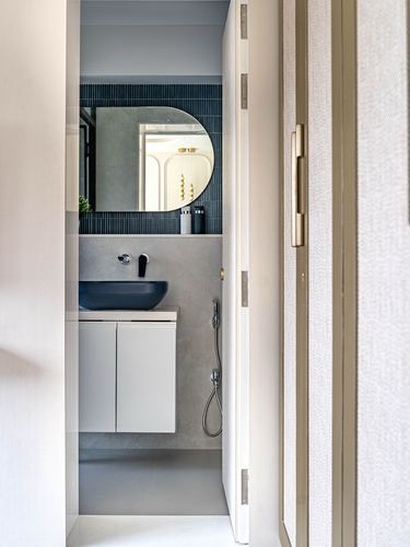 View through open door into a small bathroom with oval mirror and dark vessel sink