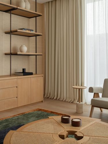 Neutral living room corner with wood shelving, cane table and sheer curtained window