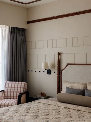 Bedroom corner with carved wood cornice, panelled wall, four-poster bed and plaid armchair