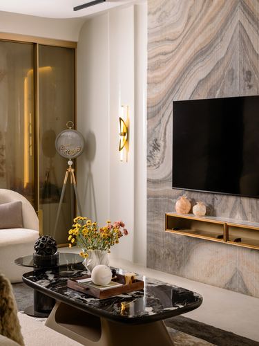 Living room with veined stone tv wall, brass console, marble coffee table and floral arrangement.