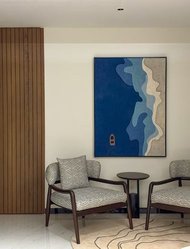 Two patterned armchairs flank a round side table beneath a large blue-toned abstract artwork on a cream wall