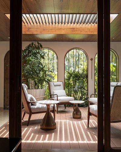 Covered veranda with cane armchairs, brass tables, and arched windows facing greenery