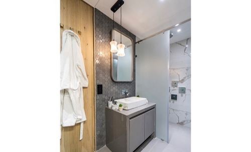 Bathroom with hexagonal tile wall, wood door with hanging robe, vessel sink vanity, and glass shower partition