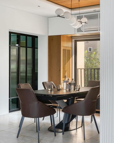 Contemporary dining room with black pedestal table, leather chairs, and slatted wood wall opening to balcony