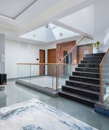 Skylit stairwell with dark stone stair treads, glass railings, and terrazzo floor in a modern home