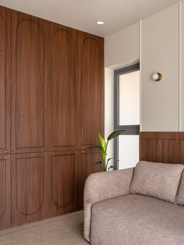 Walnut wardrobe with arched panel detailing beside a window and mauve sofa