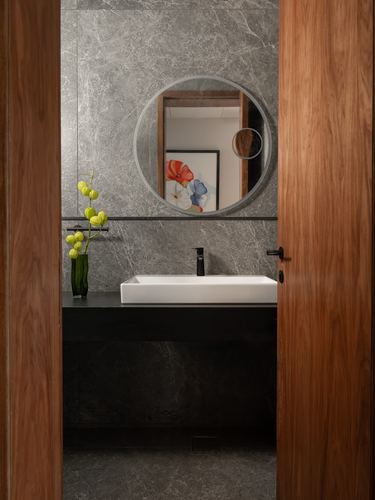 Bathroom seen through open wood door, round mirror, black stone counter, vessel sink