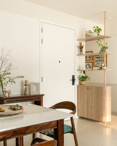 Foyer with white door, wooden shelving unit with plants and art, marble-top dining table in foreground