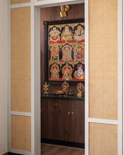 Pooja nook with Tanjore painting and brass idols framed by cane sliding doors