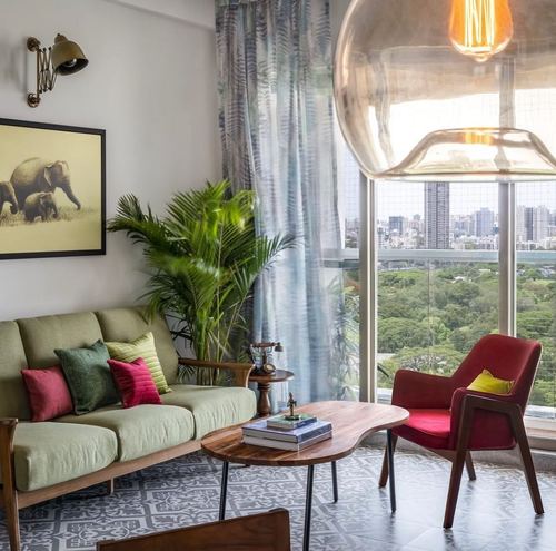 Living room with green sofa, red armchair, kidney coffee table and city view through tall windows
