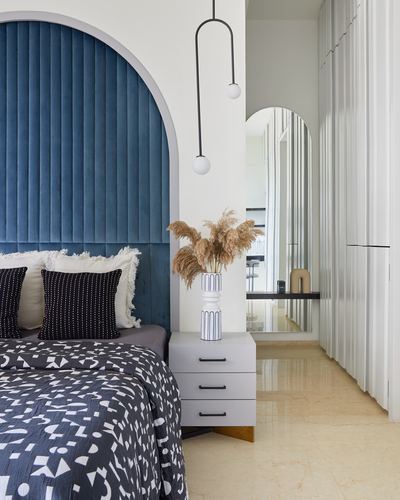 Bedroom with blue velvet arched headboard, patterned bedding, and arched mirror leading to a dressing area