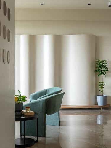 Sage velvet curved armchair before a rippled cream fluted wall panel in a stone-floored foyer