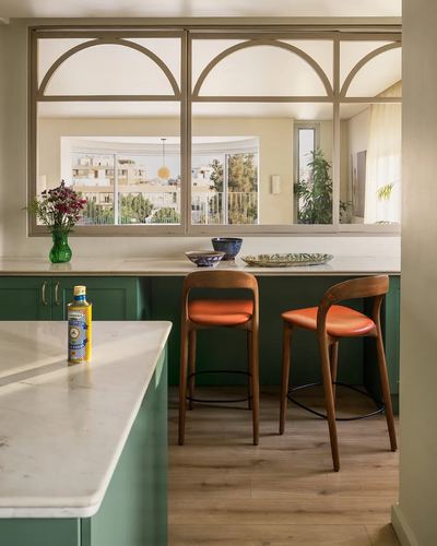 Green kitchen island with marble counters and arched windows overlooking city, orange bar stools at counter