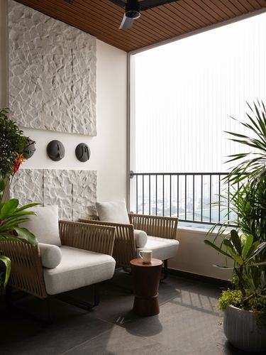 Balcony seating area with cane lounge chairs, wooden ceiling, textured stone wall, and plants overlooking city view