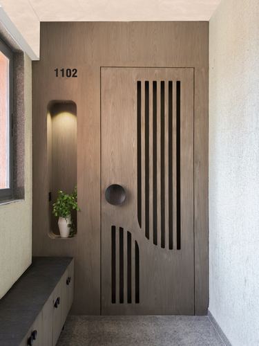 Entry door with vertical slat cutouts beside a lit wall niche holding a plant