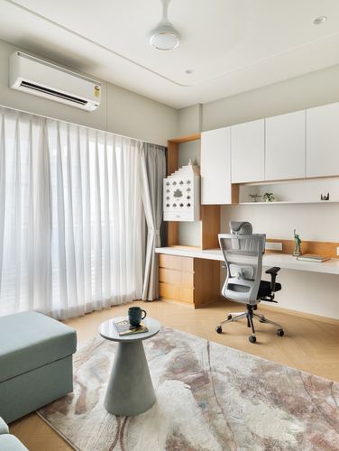 Home study nook with white desk, mesh chair, wood shelving, sheer-curtained window, and rug with round side table
