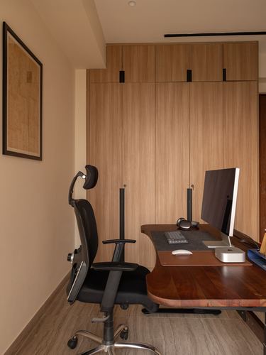 Home study nook with wood-panelled wardrobe, wooden desk, monitor, and black ergonomic chair