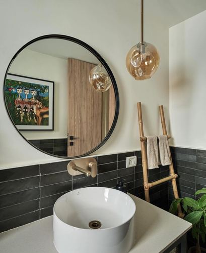 Round black-framed mirror above white vessel sink with amber glass pendant and bamboo towel ladder