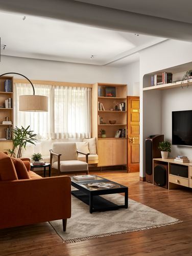 Living room with orange sofa, wood shelving, arc lamp, and arched tv niche in daylight