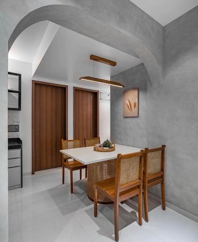 Dining nook with cane chairs, round-base table, and wooden doors under a plastered archway