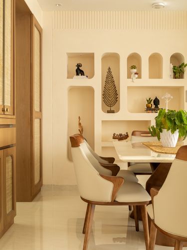 Dining nook with arched wall niches holding decor, wood-and-cane chairs around a marble-top table.