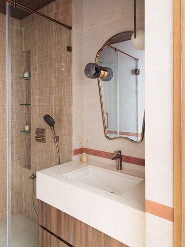 Bathroom vanity with wavy brass mirror, terracotta trim, wood cabinetry, and glass-walled shower