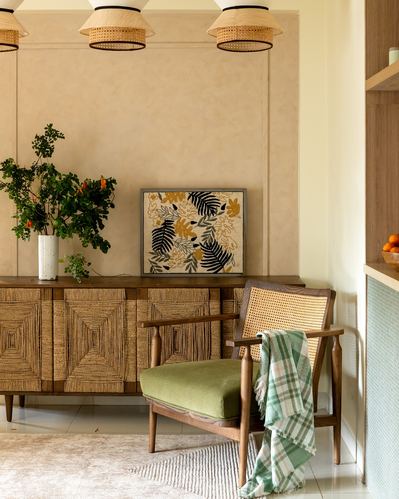 Living room corner with woven sideboard, cane armchair, and botanical art against a plastered wall
