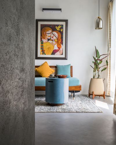 Cane sofa with teal cushions under a colorful framed portrait, seen past a concrete wall.
