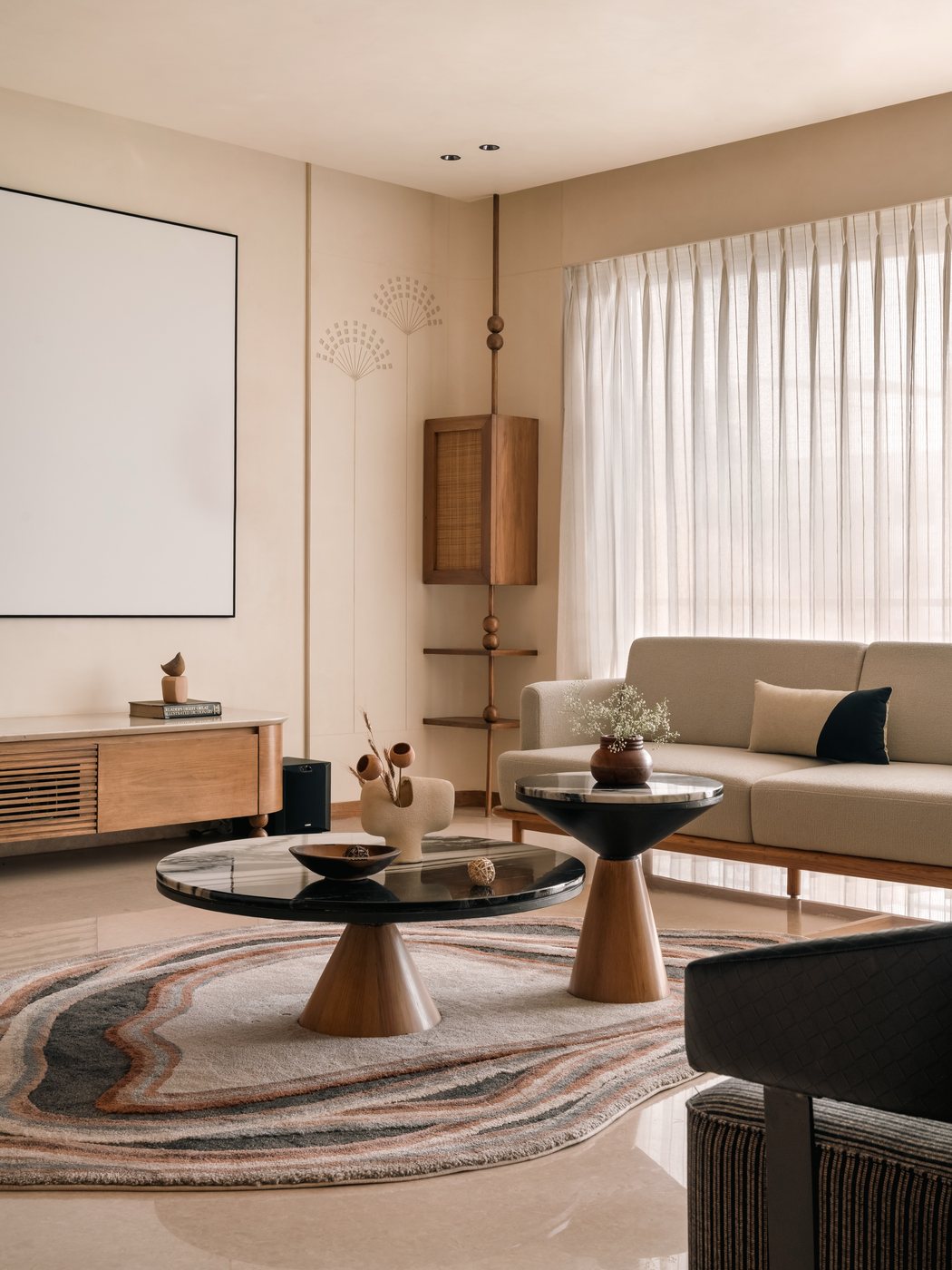 Neutral-toned living room with two round pedestal coffee tables, beige sofa, and sheer curtained window