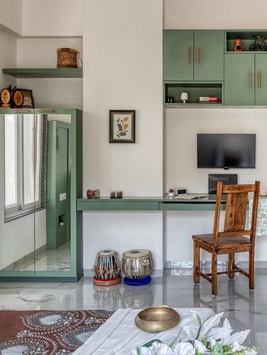 Study nook with green cabinetry, wall-mounted TV, wooden chair and tabla drums on marble floor