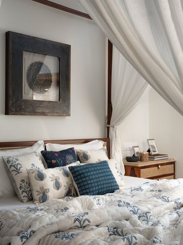 Bedroom with canopy bed, blue block-print cushions, framed artwork, and cane nightstand